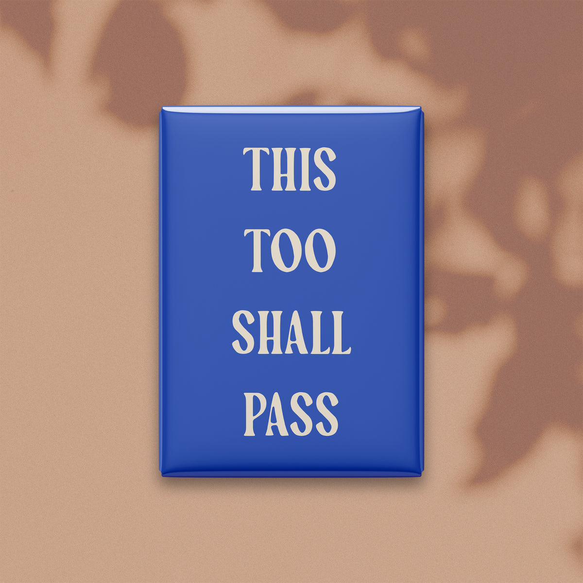This Too Shall Pass magnet in Parchment lettering on a Cobalt background, shown on a warm neutral background