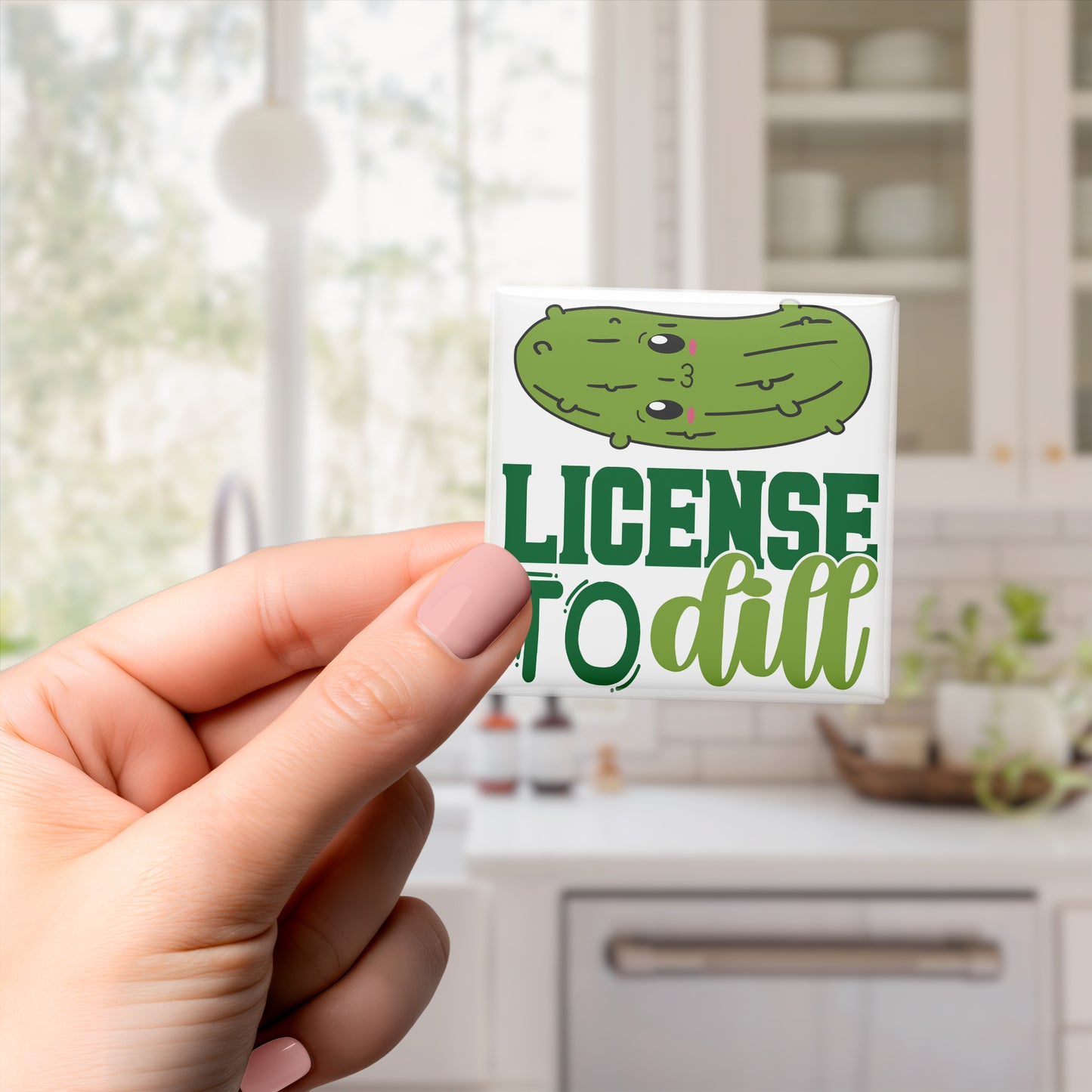 A hand holding a sticker with a cartoon pickle and the text "License to dill" printed on it.