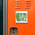 a sticker with a cartoon pickle and the text "I'm the real dill" on an orange surface.
