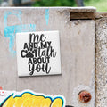 A white tile with black text that says "me and my Cott talk about you" is attached to a concrete wall.