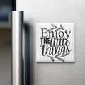 A white refrigerator magnet with the text "Enjoy the little things" in black lettering.
