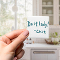 A hand holding a small white square magnet with the text "Do it lady! - Chit" written on it.