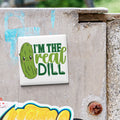 A sticker with a cartoon pickle and the text "I'm the real dill" is attached to a concrete surface.