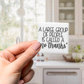 A person's hand holding a small white object with black text on it, which says "A large group of people is called a no thanks".