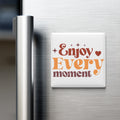 A white refrigerator magnet with the text "Enjoy Every moment" in orange and brown colors.
