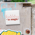 a white square magnet with the text "kindness is magic" written on it, attached to a weathered concrete wall.