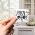 A hand holding a small square magnet with the text "CUTEST APPLE IN THE ORCHARD" on it.