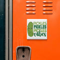 a sticker with a cartoon pickle and the text "Pickles, Pickles, Vibes" on an orange surface.