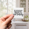 A hand holding a square magnet with the text "NOPE not today" on it.