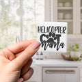 A hand holding a small square magnet with the text "HELICOPTER CUT MAMA" printed on it.