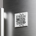 A white square magnet with the text "Enjoy the little things" on it is attached to a metallic surface.