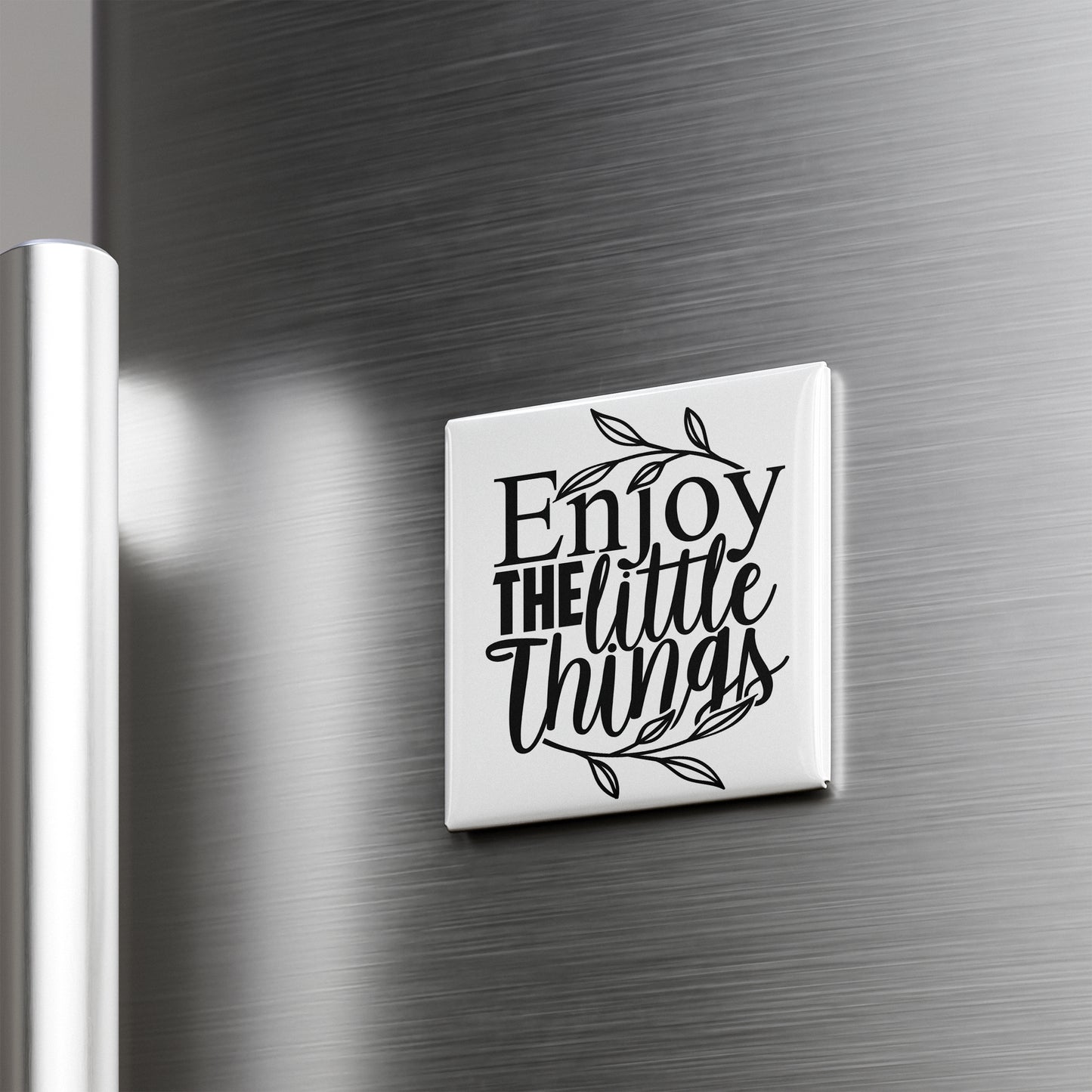 A white square magnet with the text "Enjoy the little things" on it is attached to a metallic surface.