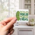 A hand holding a sticker with a cartoon pickle and text that says "Pickles, Pickles, Vibes".