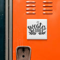 a bright orange surface with a white square sign that says "sweater weather" in black text.
