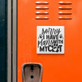 a sticker with the text "Sorry I HAVE plans with my cat" on an orange surface, which appears to be a locker or a similar storage unit.