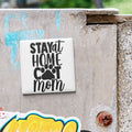 A white sticker with the text "STAY AT HOME COT MOM" is attached to a concrete surface.
