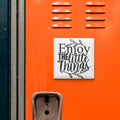 a vibrant orange wall with a motivational quote in black text that reads "Enjoy the little things".