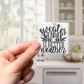A hand holding a small white object with black text that says "sweater weather is better".