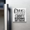 A white refrigerator magnet with black text that reads "Free Hugs Just Kidding Don't Touch Me".
