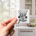 A hand holding a small square magnet with the text "CAT HAIR IS MY GLITTER" on it.
