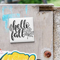 a white square magnet with the text "Hello fall" written on it, placed on a weathered concrete surface.
