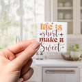 A hand holding a small white object with text on it, which appears to be a magnet or sticker.