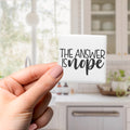 A hand holding a small square magnet with the text "THE ANSWER IS NOPE" written on it.