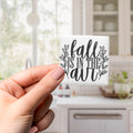 A hand holding a small square magnet with the text "fall is in the air" written on it.