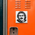 a sticker of a man's face on an orange surface, with a metal vent and a small object below it.