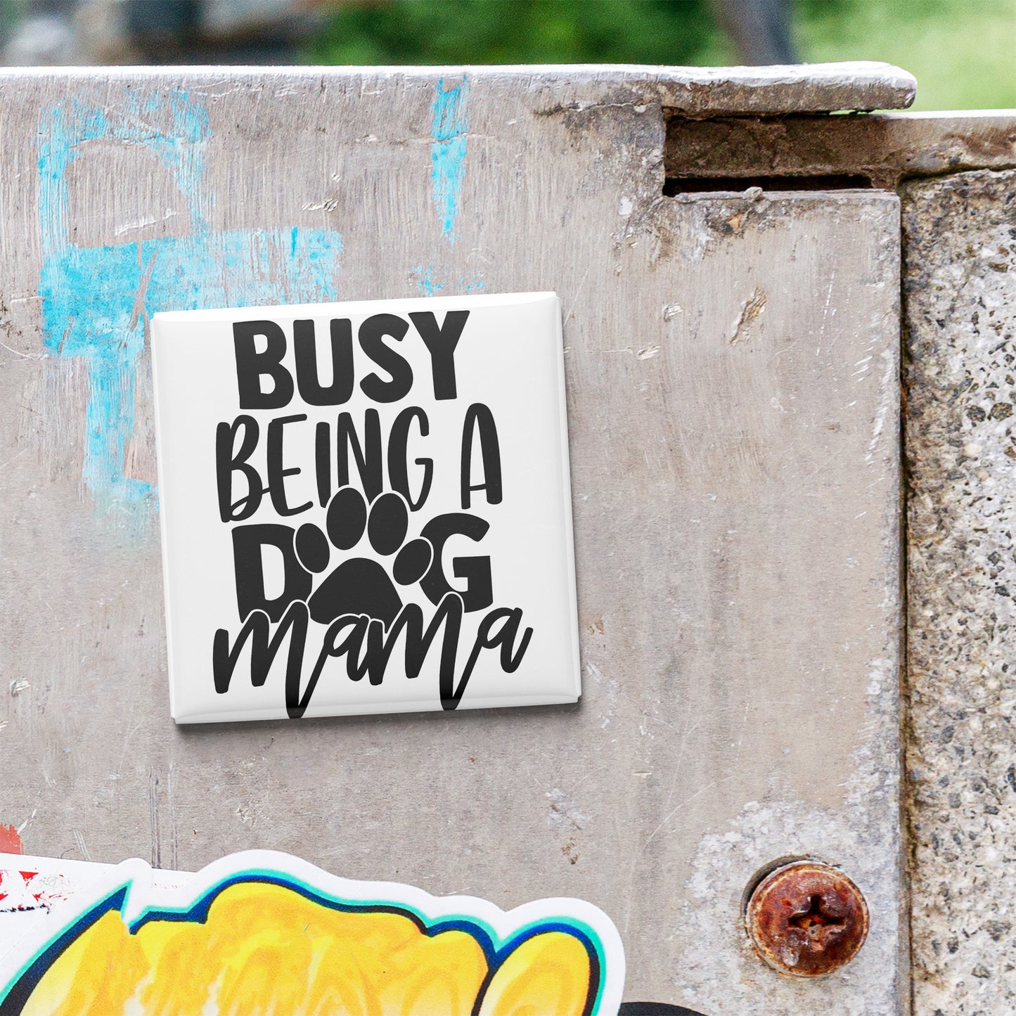 A sticker with the text "BUSY BEING A DOG MAMA" is attached to a concrete surface.