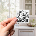 A hand holding a small white sticker with black text that says "Sorry I have plans with my cat".