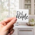 A hand holding a small square magnet with the text "EW... people" written on it.